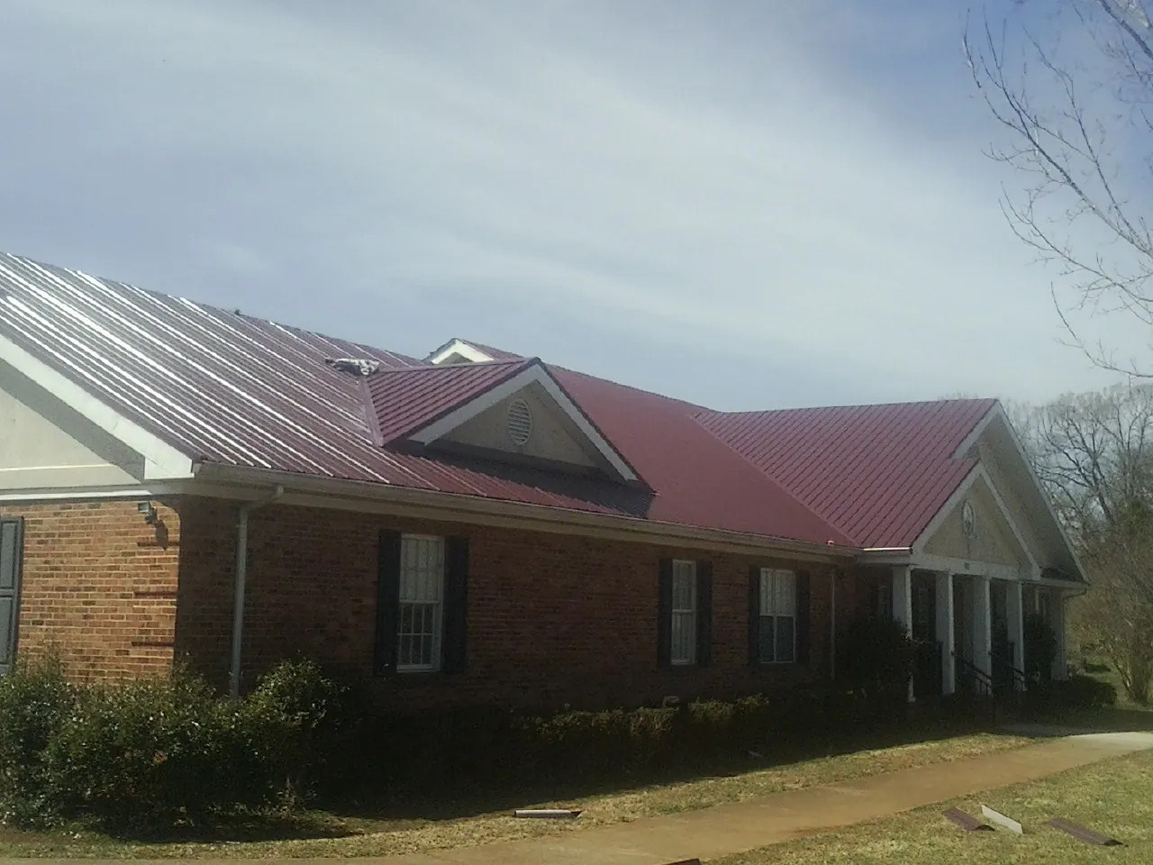 Red metal roof with gabled entries on a long brick building, from a Hail Damage Roof Repair job in Melbourne Beach