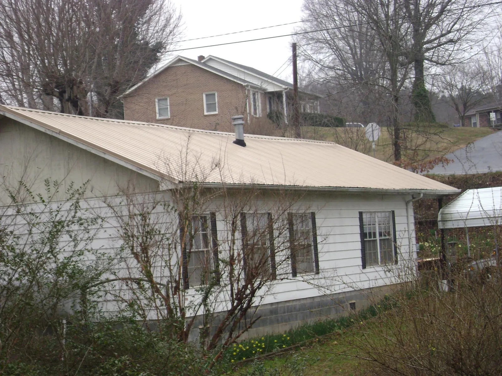 Tan metal roof on a white sided house set into a hillside — Commercial Roofing by Roofing Brothers in Melbourne Beach